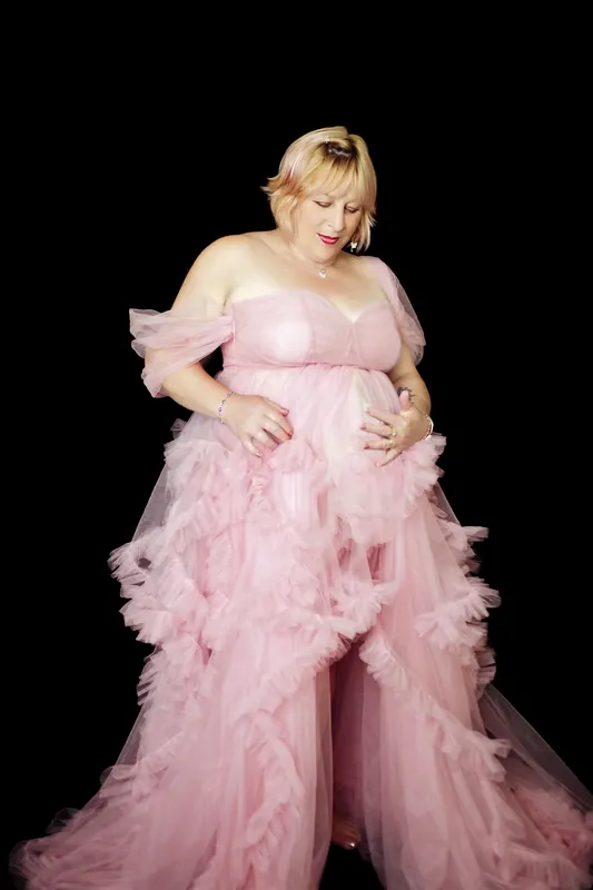 Schwangere Frau im rosa Tüllkleid, Hände am Bauch