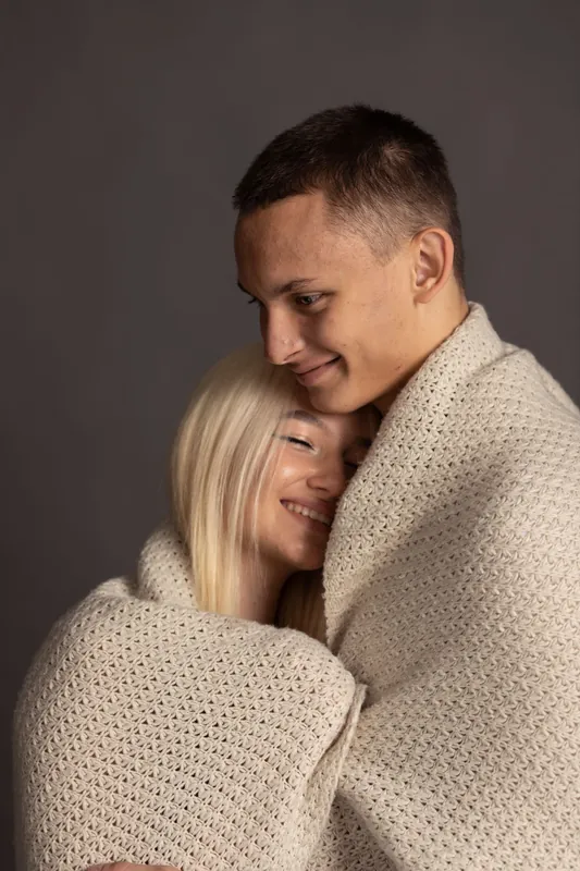 Paar eng in eine Strickdecke gekuschelt, Studioporträt